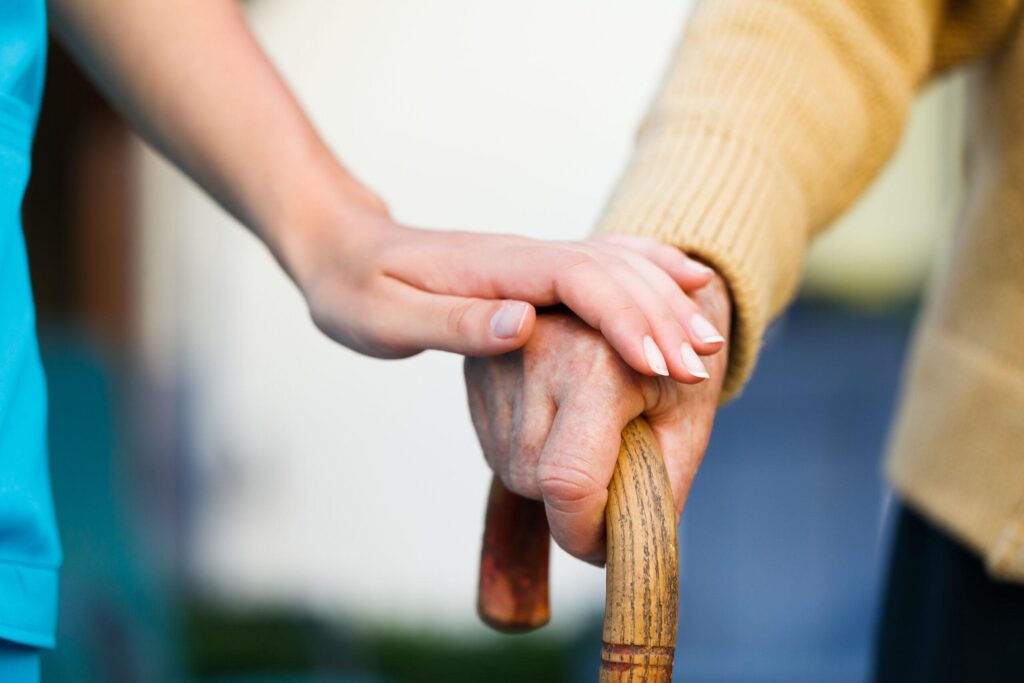 resident holding walking stick with carers comforting hand on top